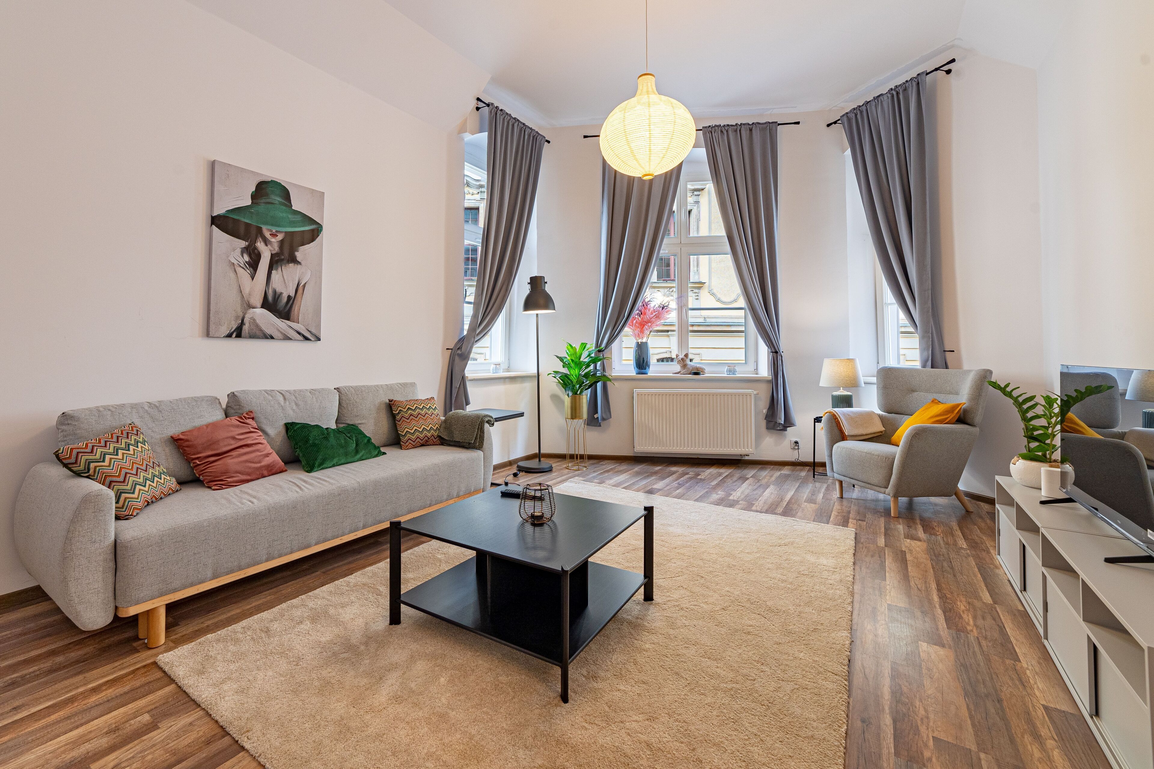 Una sala de estar moderna con un sofá gris, una mesa de centro negra y un sillón gris. Hay un cuadro en la pared, una lámpara de pie y una planta en maceta.