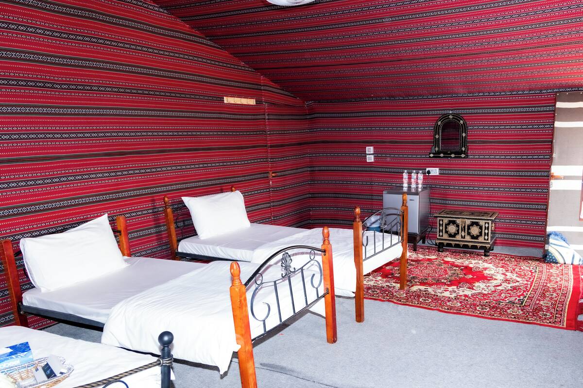 A room with two beds, a small table, a mirror, and a radiator.