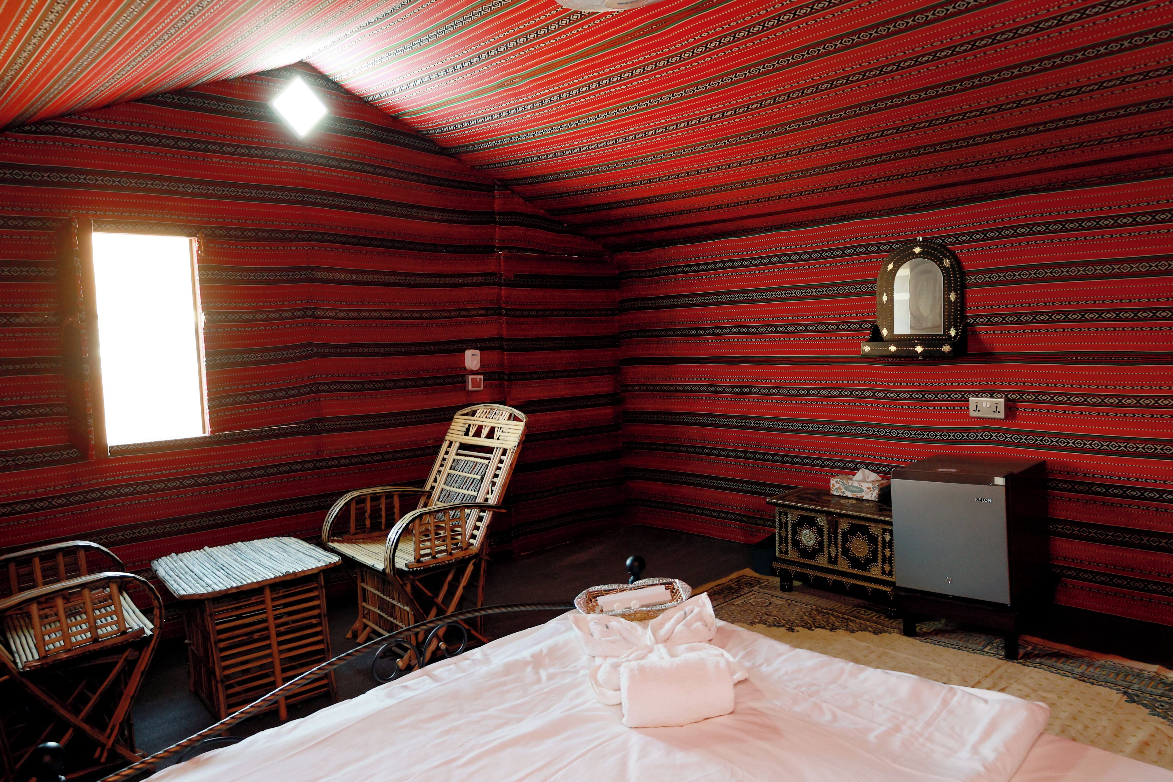 A room with a bed, a chair, a small table, a mirror, and a cabinet.
