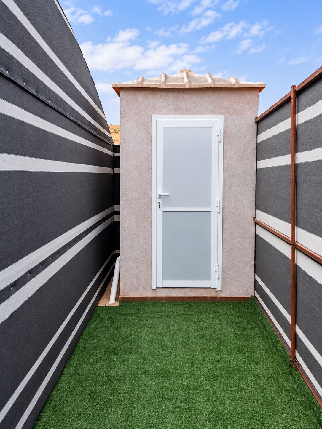 A small, enclosed space with a door, artificial grass flooring, and striped walls.