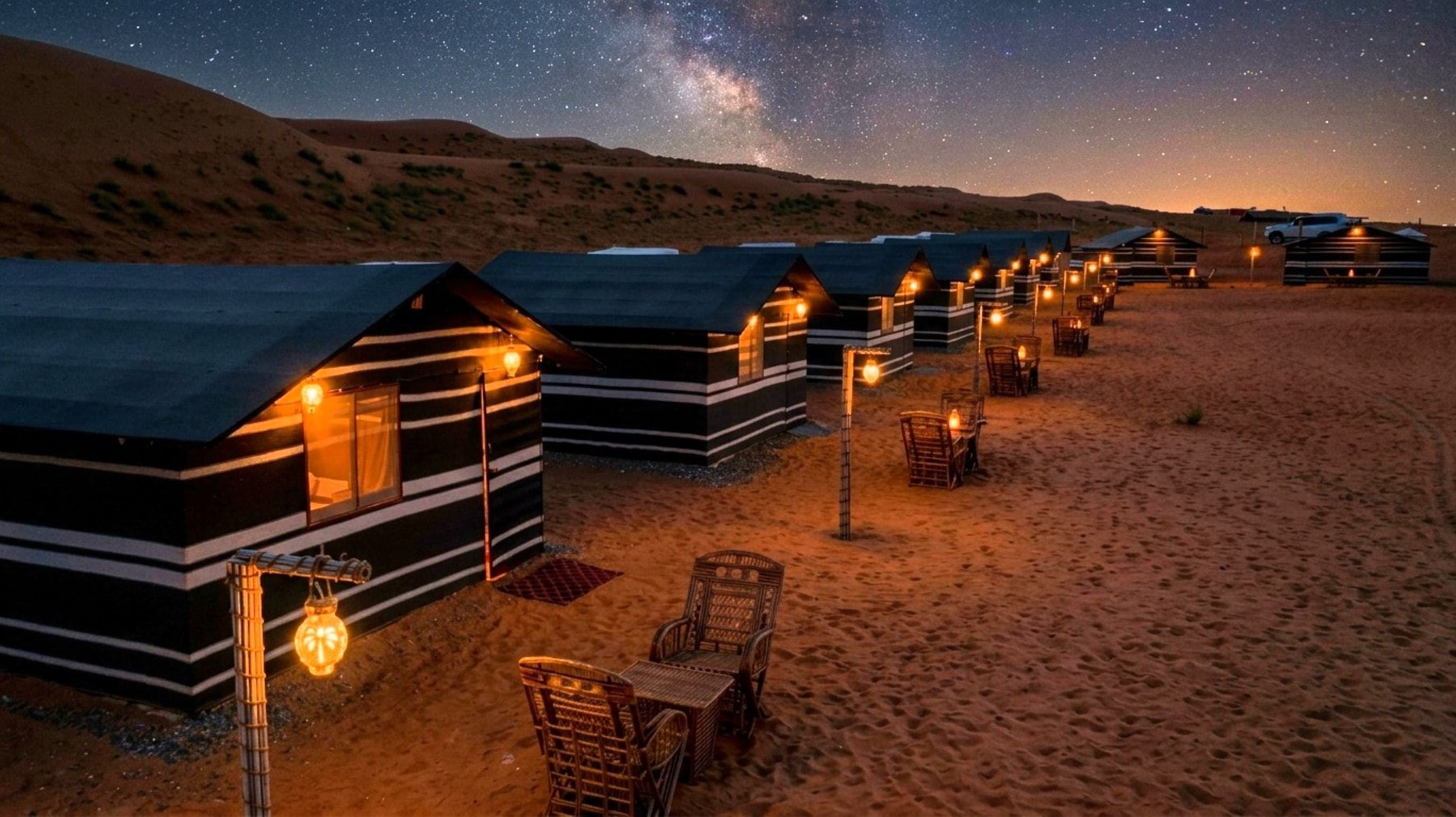A row of cabins with a starry night sky above, arranged on a sandy terrain.