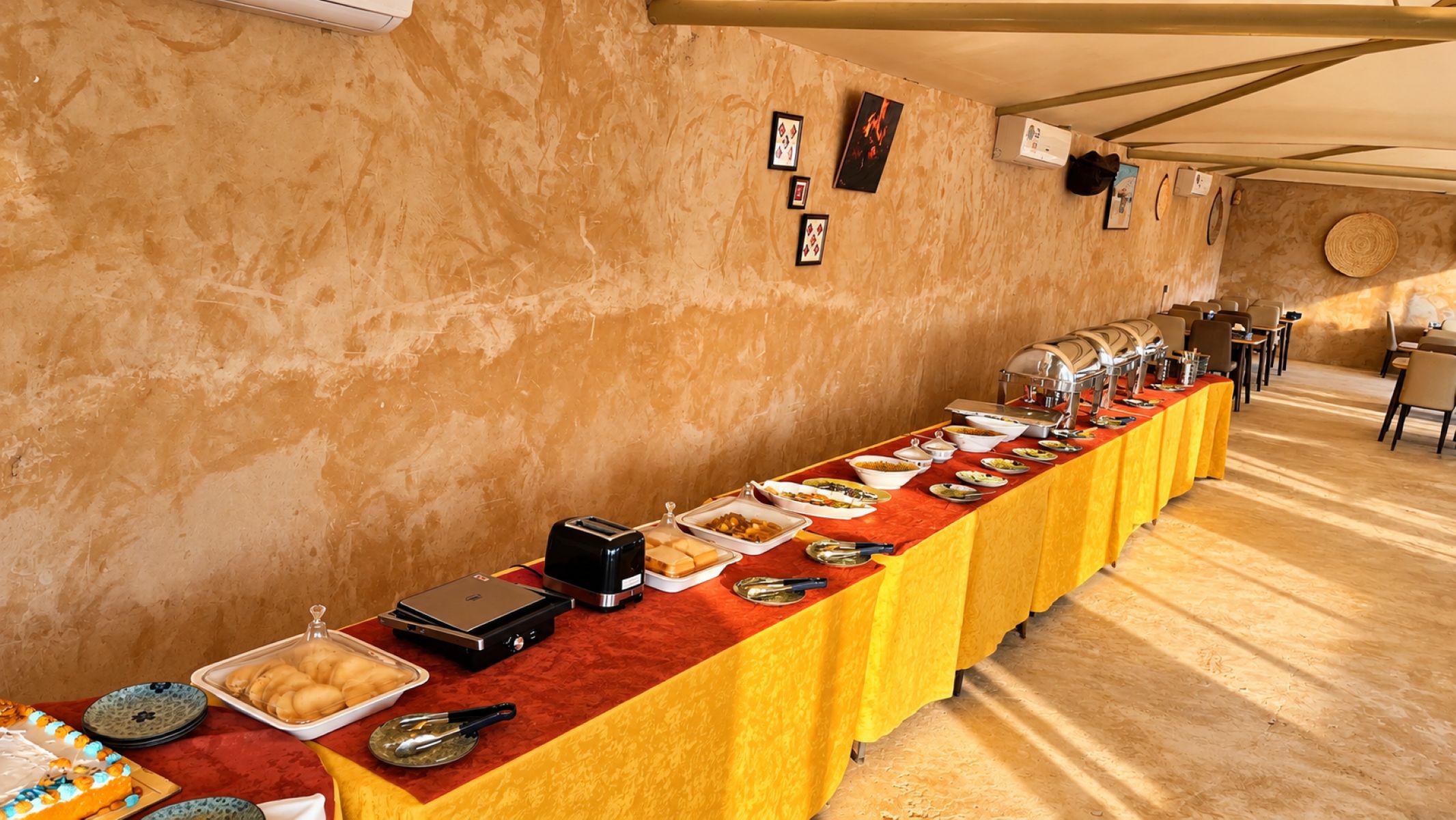 Montaje de bufé con diversos alimentos y una larga mesa cubierta con un mantel amarillo.