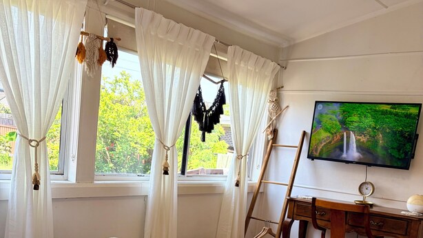 A neatly arranged bedroom with a bed, a desk, a television, and a window with curtains.