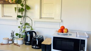 A kitchen counter with a toaster, kettle, microwave, and jars of condiments.