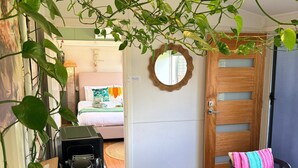 A cozy room with a bed, a coffee maker, a chair with a colorful throw, and a wooden door.