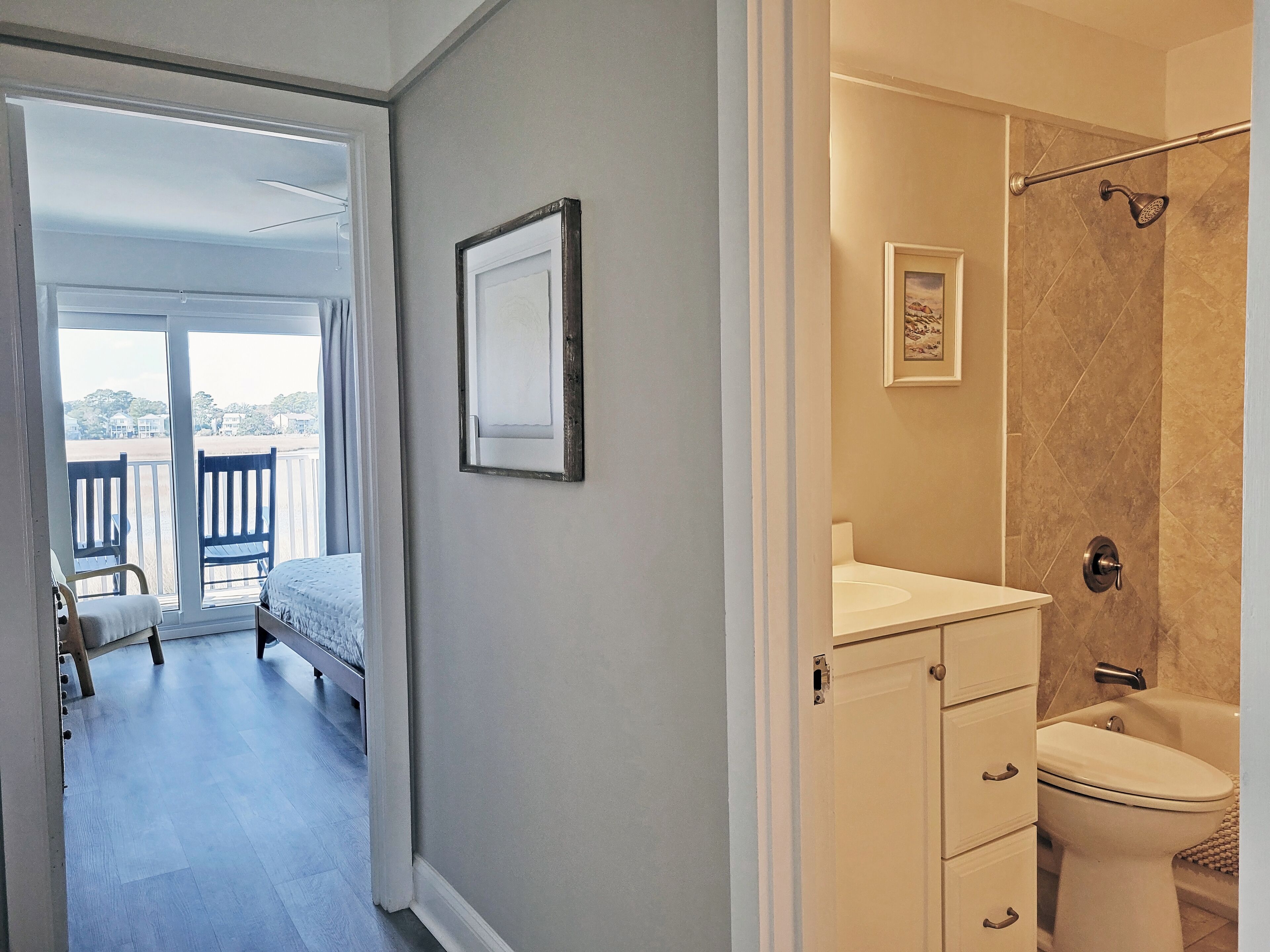 A bedroom with a bed, a window with a view of the beach, and a bathroom with a shower and toilet.