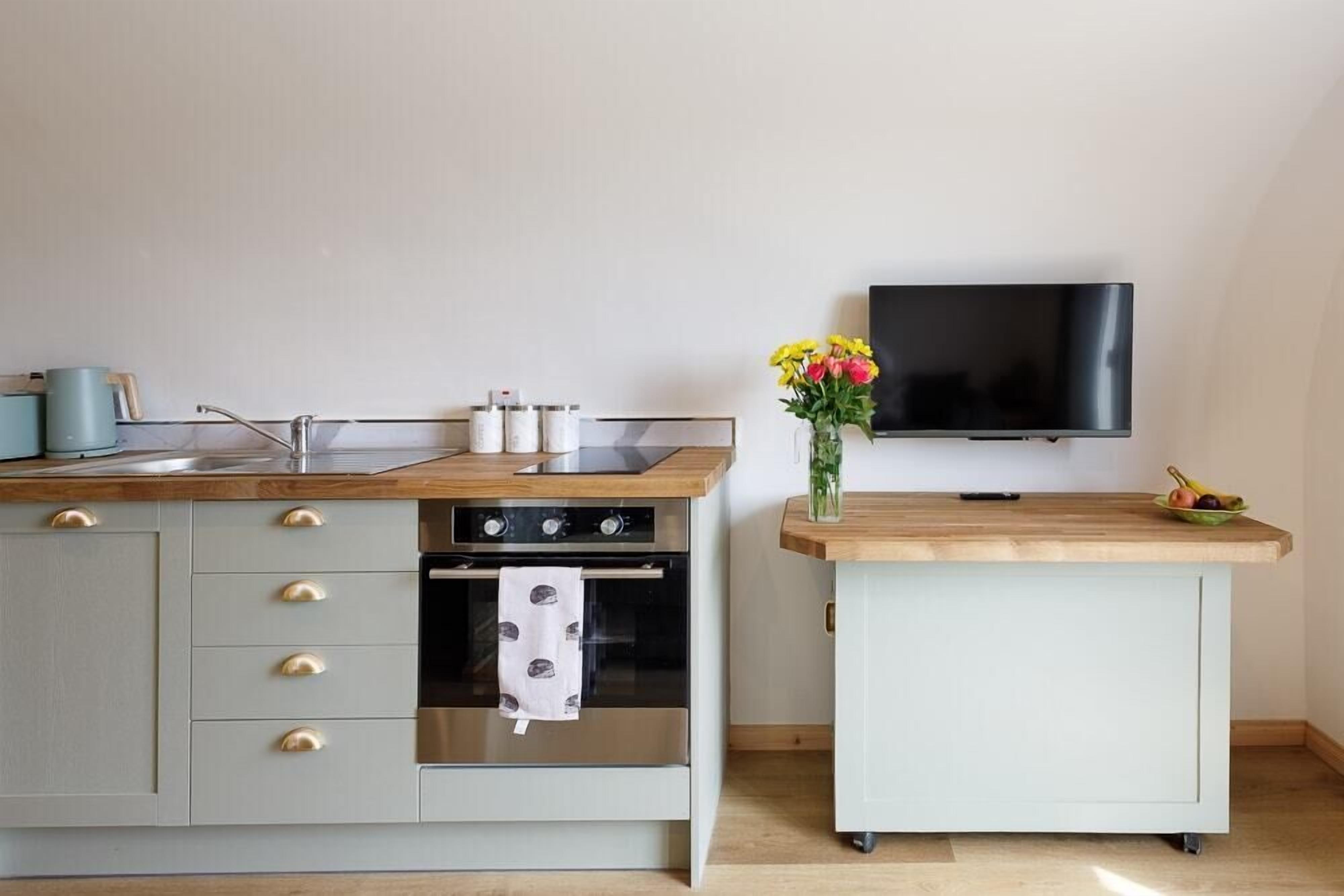 Une cuisine compacte dotée d’un plan de travail en bois, d’un four encastré, d’un petit placard et d’un téléviseur fixé au mur.