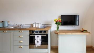Une cuisine compacte dotée d’un plan de travail en bois, d’un four encastré, d’un petit placard et d’un téléviseur fixé au mur.