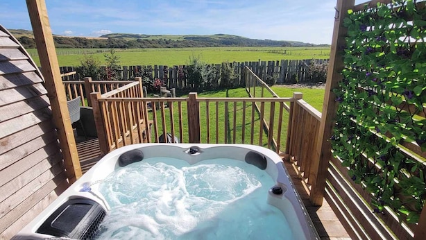 Ein Whirlpool unter einer Hollaube mit Blick auf ein grünes Feld und Hügel.