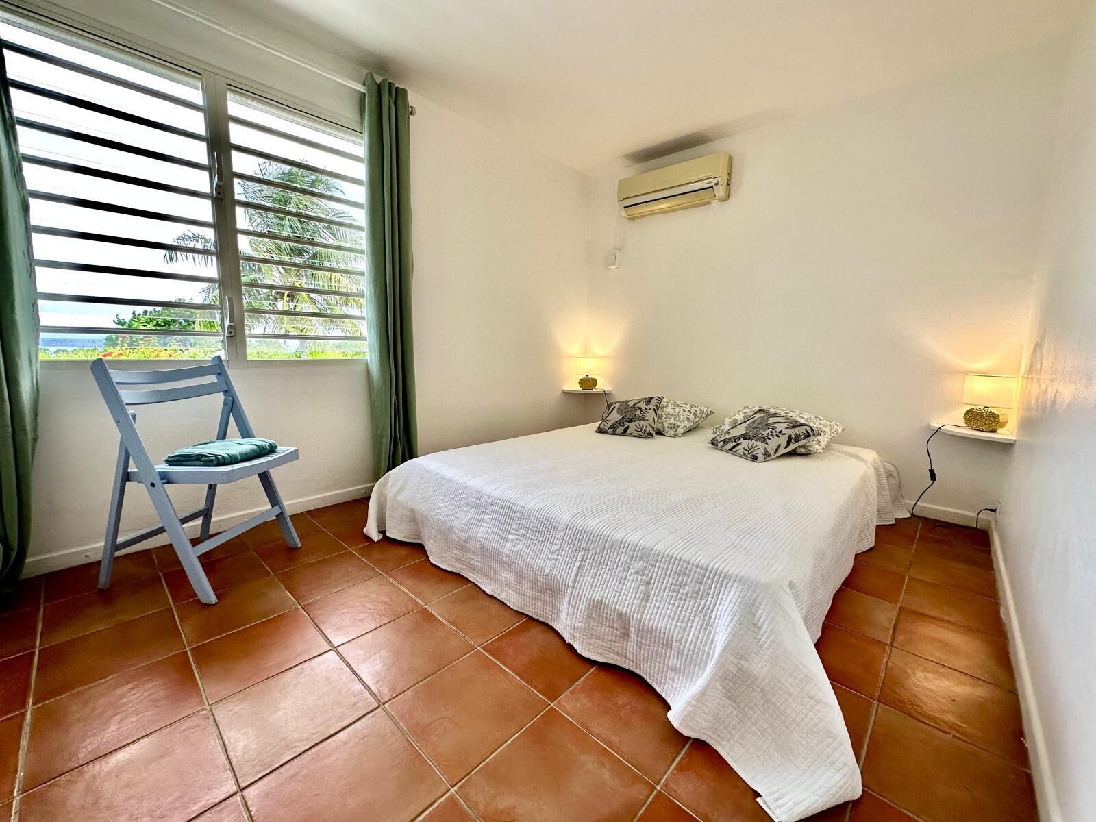 Un dormitorio con cama, una silla, ventana con cortinas, aire acondicionado y lámparas de pared.