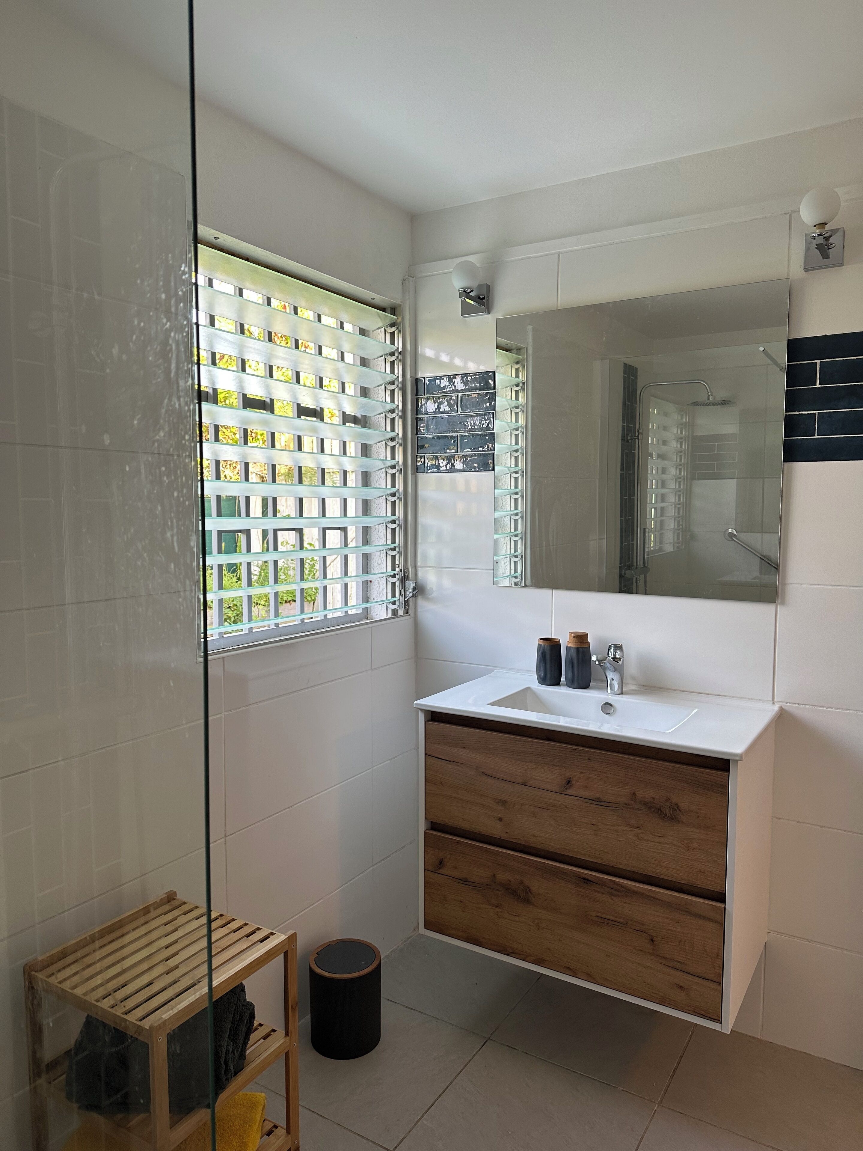 A modern bathroom with a glass shower enclosure, a white sink with wooden drawers, and a large mirror above it.