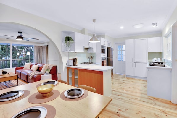 A modern kitchen with white cabinets, a central island, and a dining area with a wooden table and chairs.
