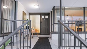 Ein moderner Eingangsbereich mit einer dunklen Holztür, einer schwarzen Fußmatte und einer Treppe mit Metallgeländern.