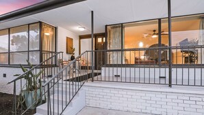 Ein modernes Haus mit überdachter Veranda, großen Fenstern und einer Treppe, die zum Eingang führt.
