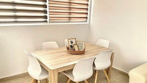 Un comedor con una mesa de madera, sillas blancas y un cesto de fotografías enmarcadas.