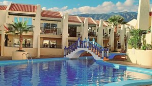 Una piscina con un puente, rodeada de edificios con balcones y palmeras.