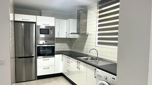 Una cocina compacta con un refrigerador de acero inoxidable, horno empotrado, microondas, lavamanos y lavadora.