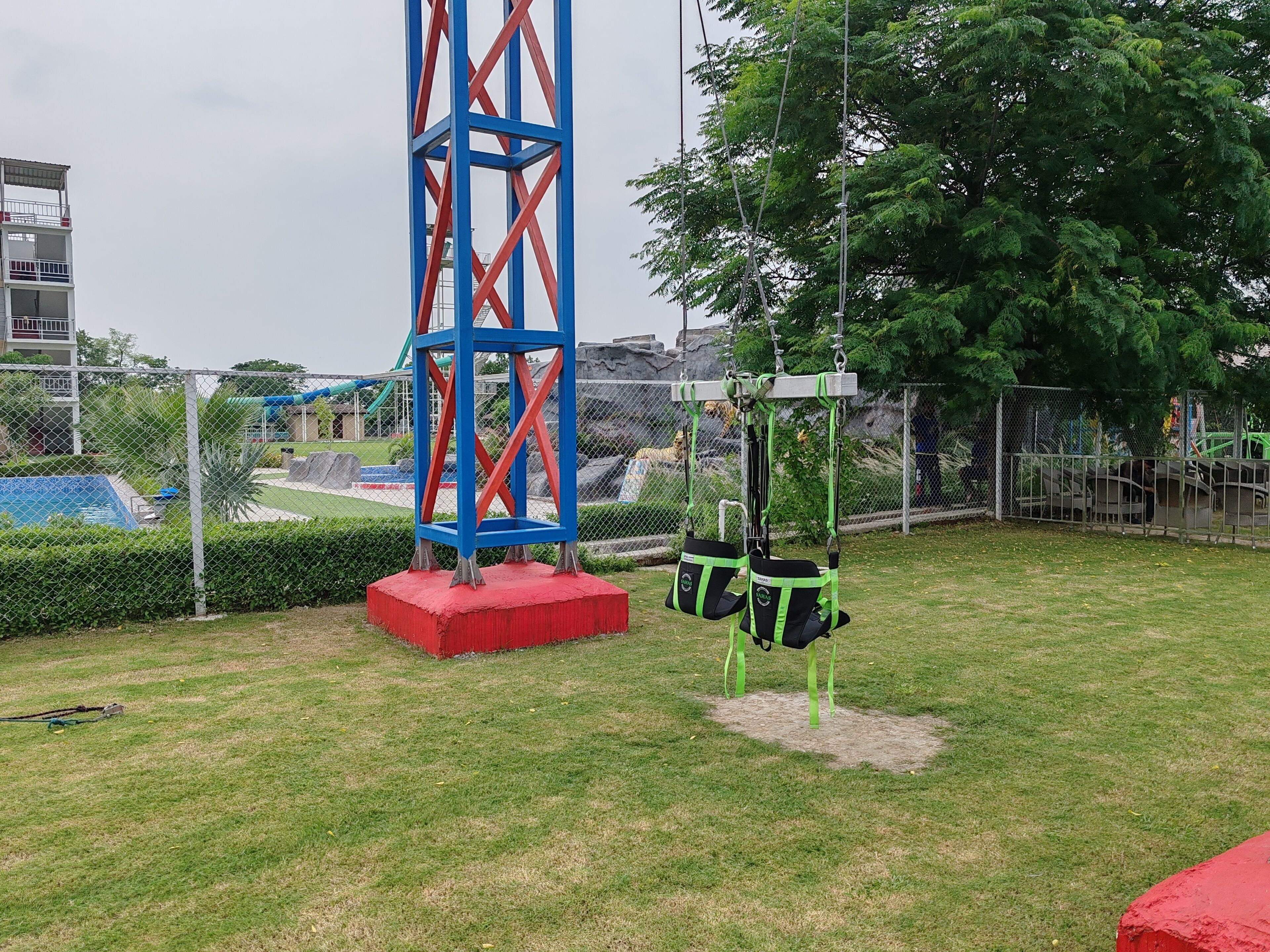 Ein Spielplatz mit einer hohen, blau und rot gestreiften Konstruktion, Schaukeln und einem eingezäunten Bereich.