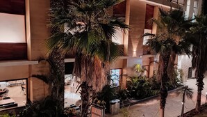 A multi-level hotel atrium with palm trees, a stone floor, and a central walkway. - The Maasai Mara Resort Water and Adventure Park Corbett (Ramnagar)