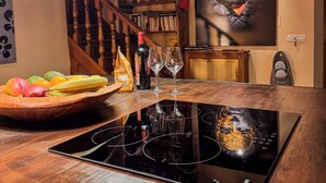 Una mesa de comedor de madera con una placa de cocina por inducción negra, un cuenco de fruta, copas de vino y una lámpara colgante.