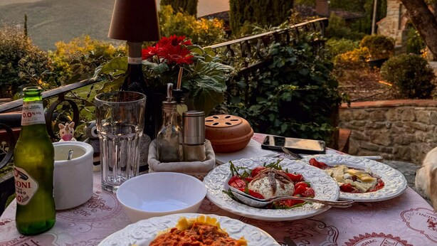 Mesa al aire libre con platos de comida, una botella de licor y vista al atardecer.