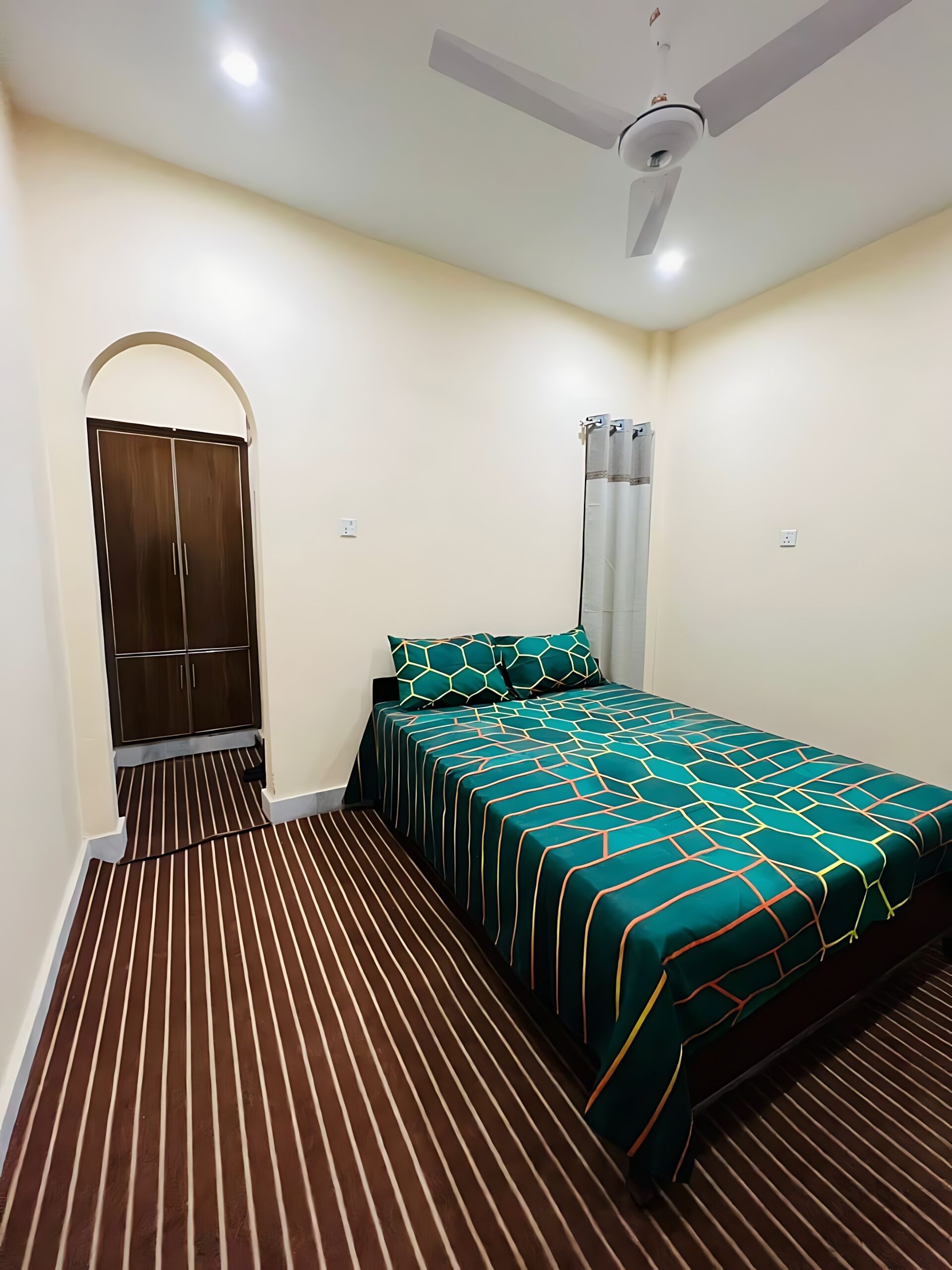 Un dormitorio con cama, armario, ventilador de techo y suelo a rayas.