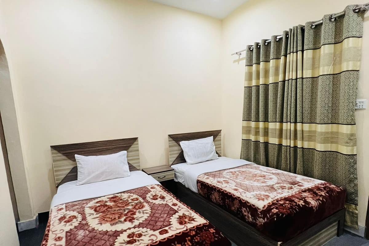 Una habitación de hotel con dos camas individuales, un ventilador de techo y una cortina estampada con diseño de cuadros.