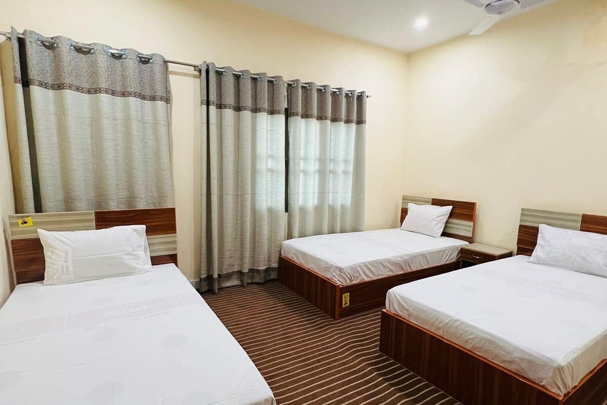 Habitación de hotel con tres camas individuales, ventilador de techo y cortinas.