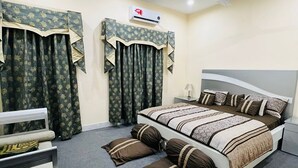A bedroom with a bed, two bedside tables, a chair, a ceiling fan, and an air conditioning unit.