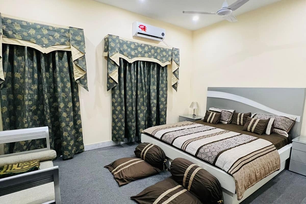 Un dormitorio con cama, dos mesitas de noche, una silla, ventilador de techo y aire acondicionado.
