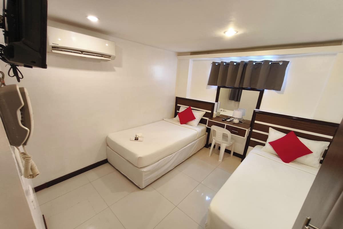 Een hotelkamer met een bed, een bureau, een stoel, een airconditioner en een televisie.
