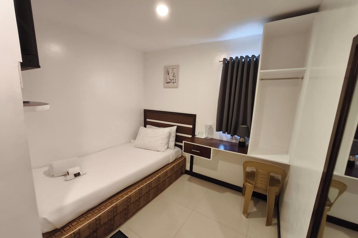 Een compacte, verzorgde slaapkamer met een enkel bed, een bureau, een stoel en een kledingkast.