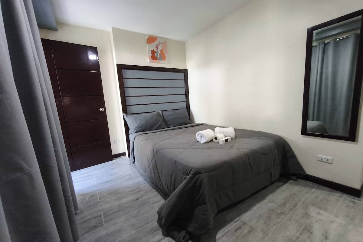 Een slaapkamer met een bed, hoofdeinde, wanddecoratie, een raam met gordijnen en een deur.