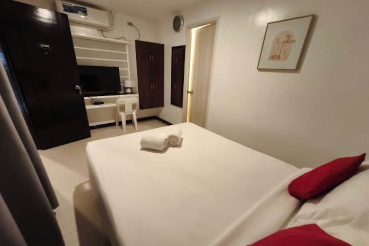A hotel room with a bed, a desk, a chair, and a wardrobe.