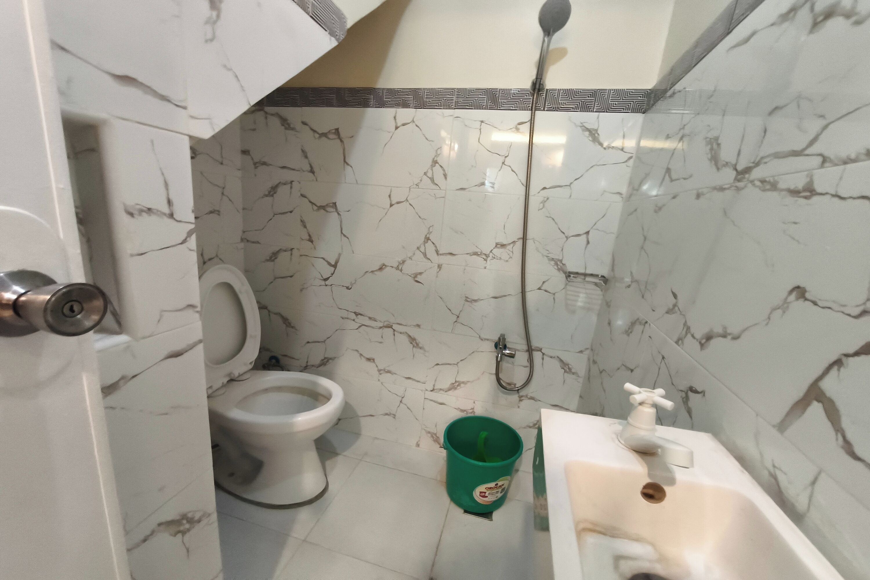 Une salle de bain avec des toilettes, un seau vert et un lavabo avec un robinet.