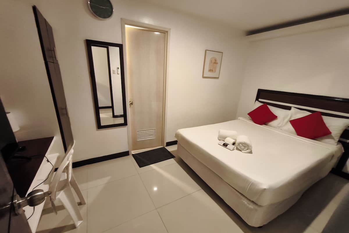 Een hotelkamer met een bed, bureau, stoel, deur en een klok aan de muur.