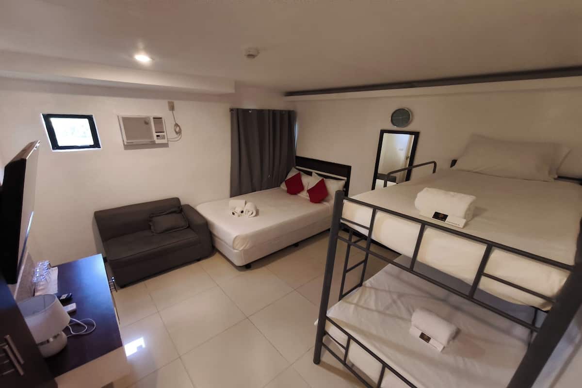 Een hotelkamer met een stapelbed, een slaapbank, een bureau met een computer en een televisie.