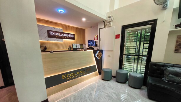 A reception area with a wooden reception desk labeled "Ecoland 88 Apartelle & Suite" and a black leather sofa. - Ecoland 88 Apartelle and Suite near SM Davao (Davao)