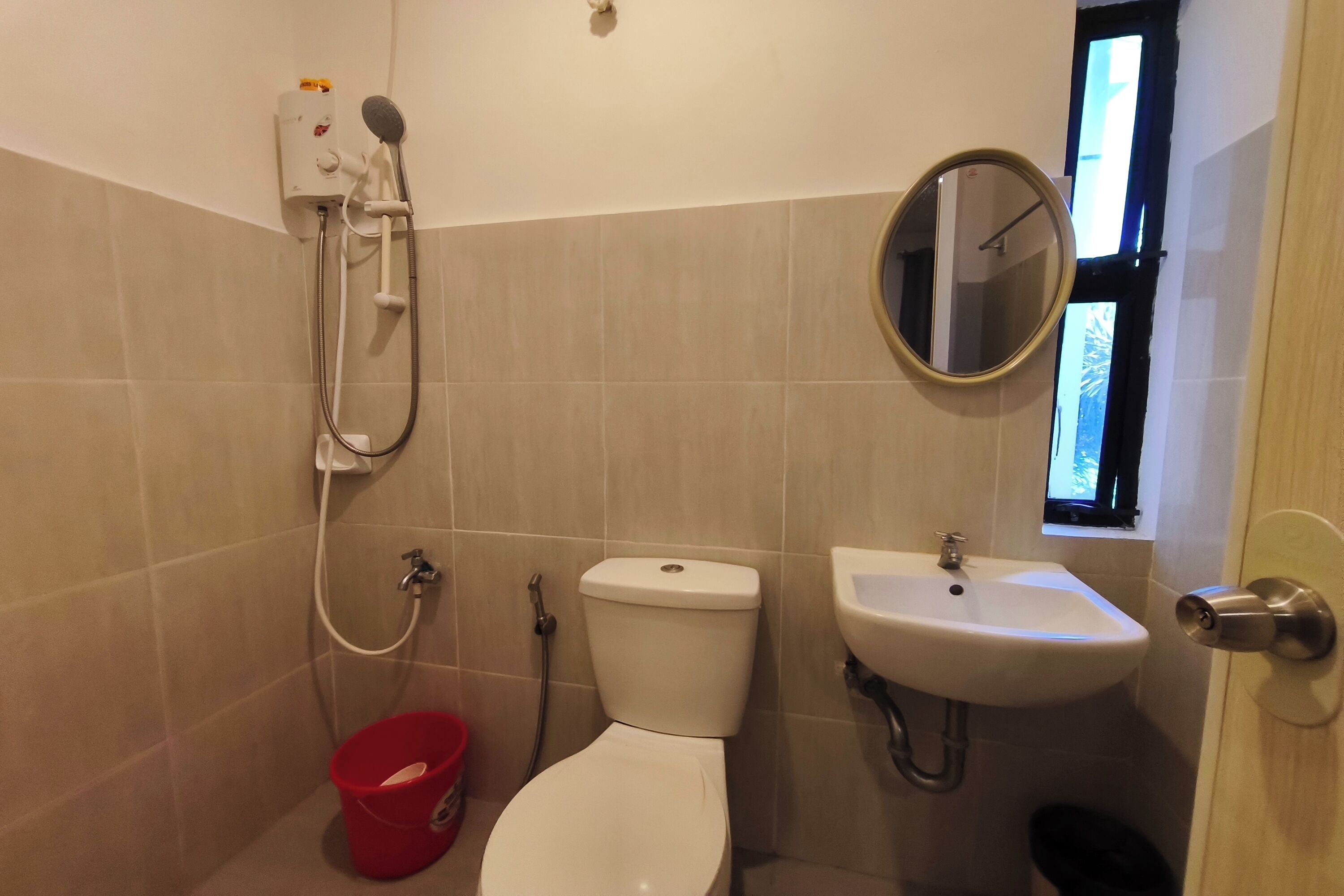 A bathroom with a toilet, a sink, a shower unit, and a window.