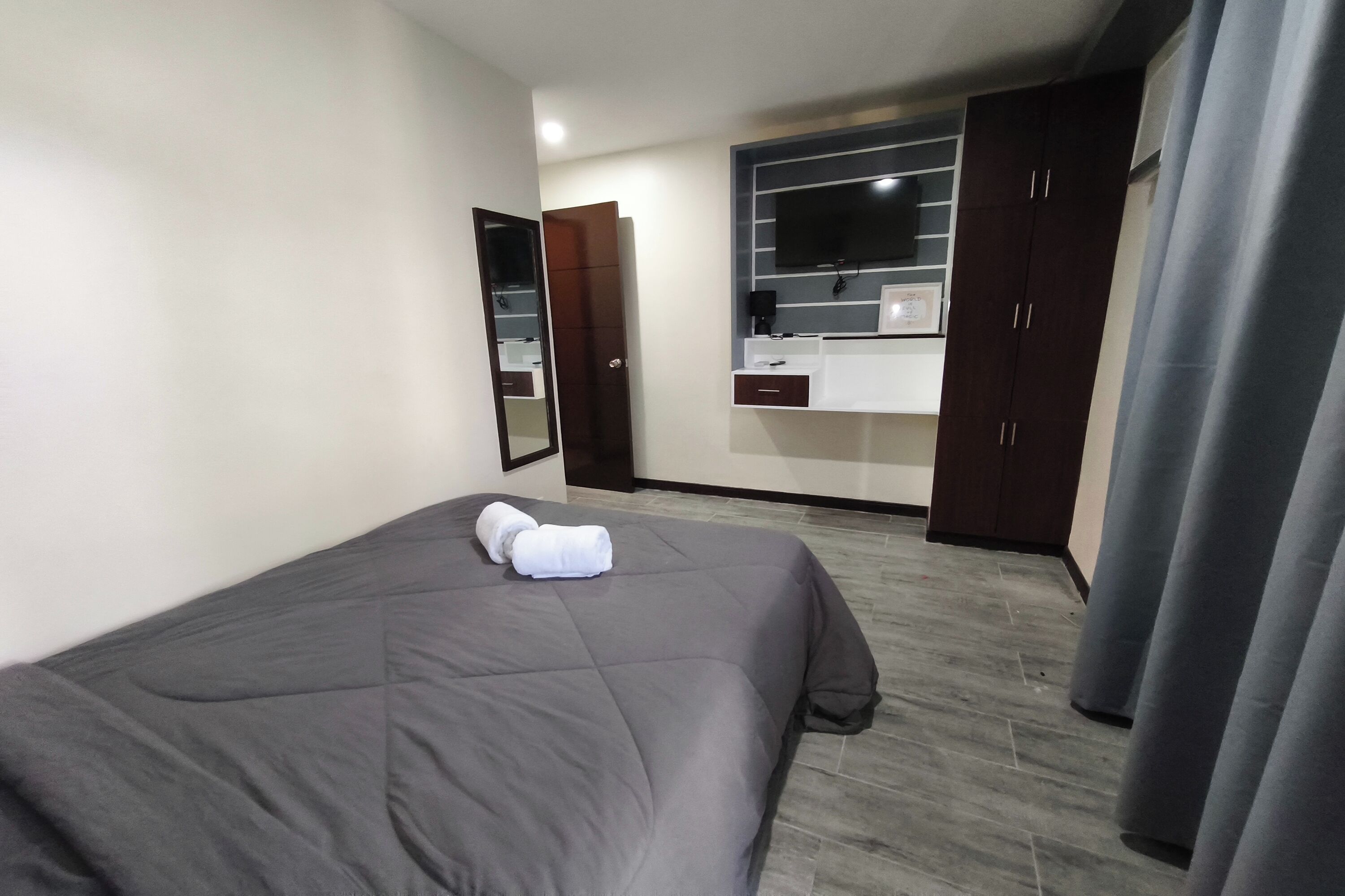 A bedroom with a bed, a wardrobe, a mirror, and a TV mounted on the wall.