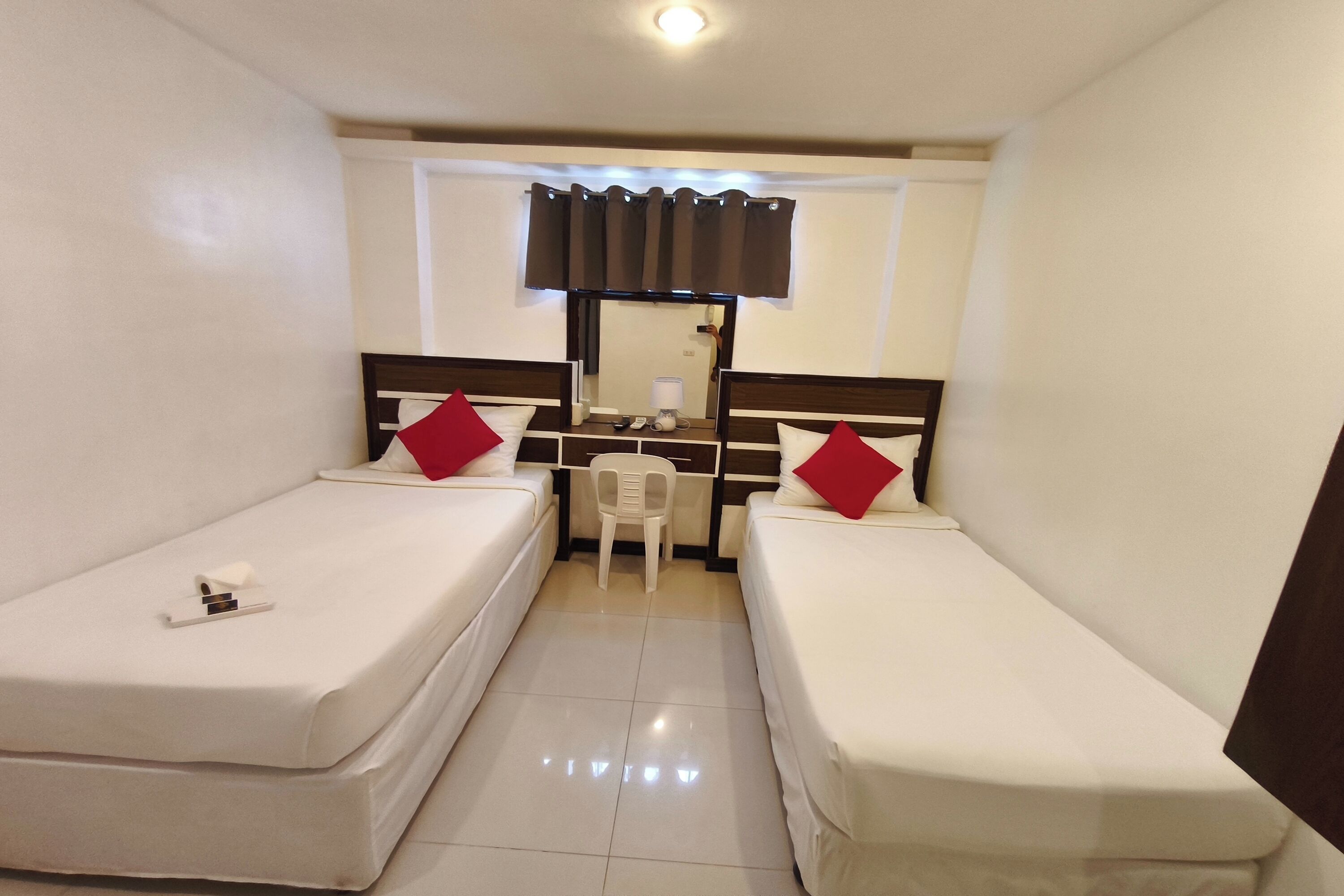 A small, clean room with two single beds, a desk, a chair, and a mirror.