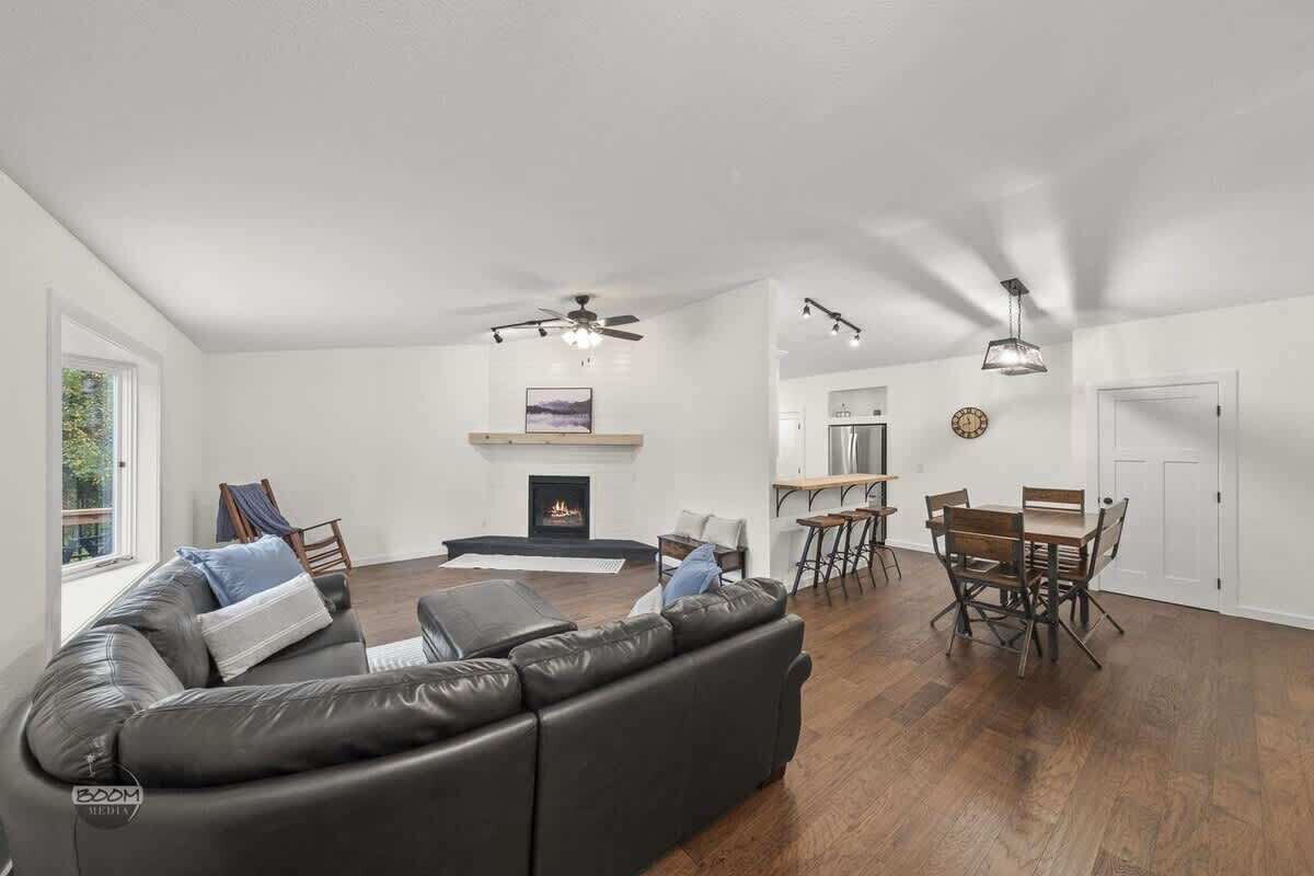 Un vaste espace de vie comprenant un canapé en cuir noir, une cheminée, une table à manger avec des chaises et un ventilateur de plafond.