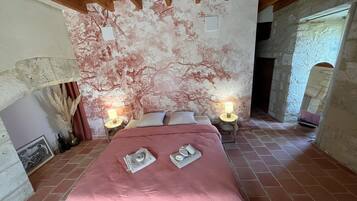A bedroom with a large bed, two bedside lamps, a wall mural, and a rustic stone wall.