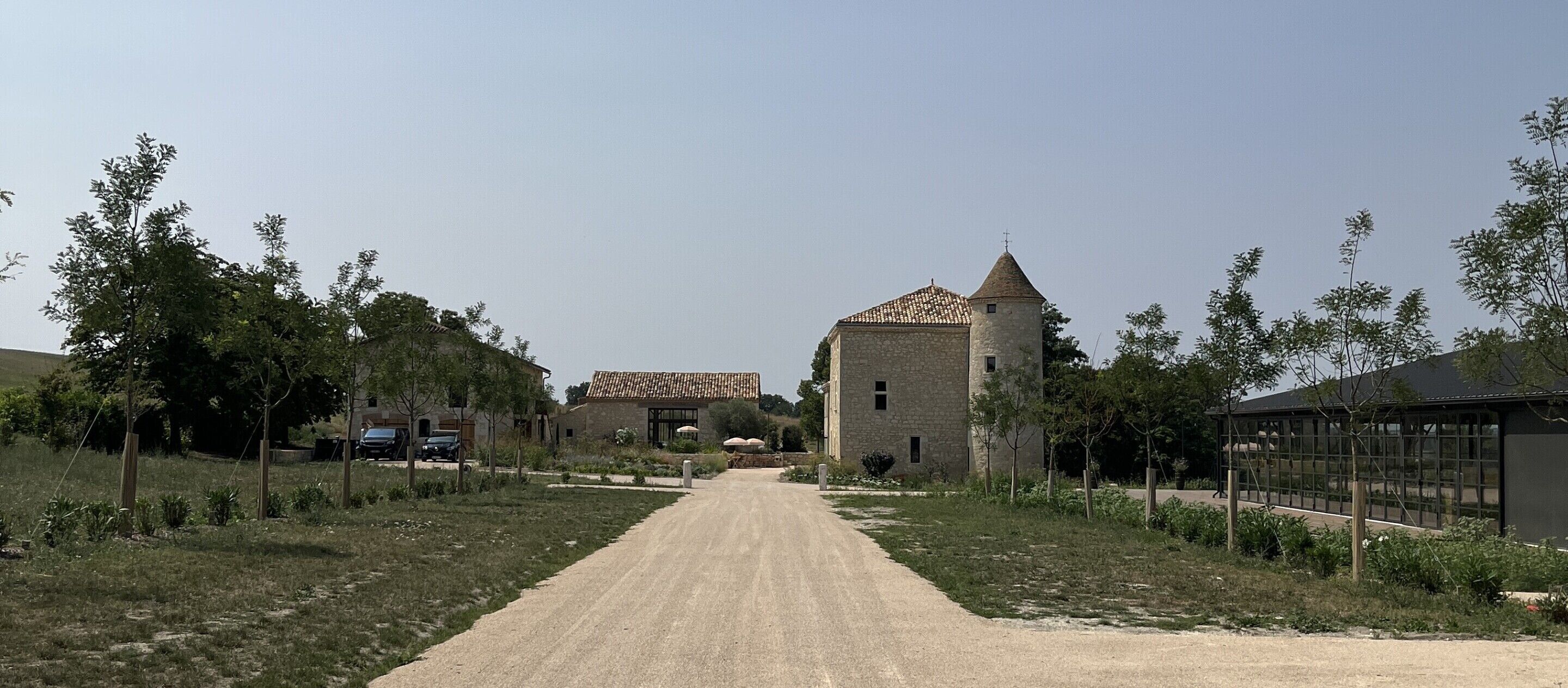 Un camino rural que lleva a un edificio de piedra con torre, rodeado de árboles y una cerca.