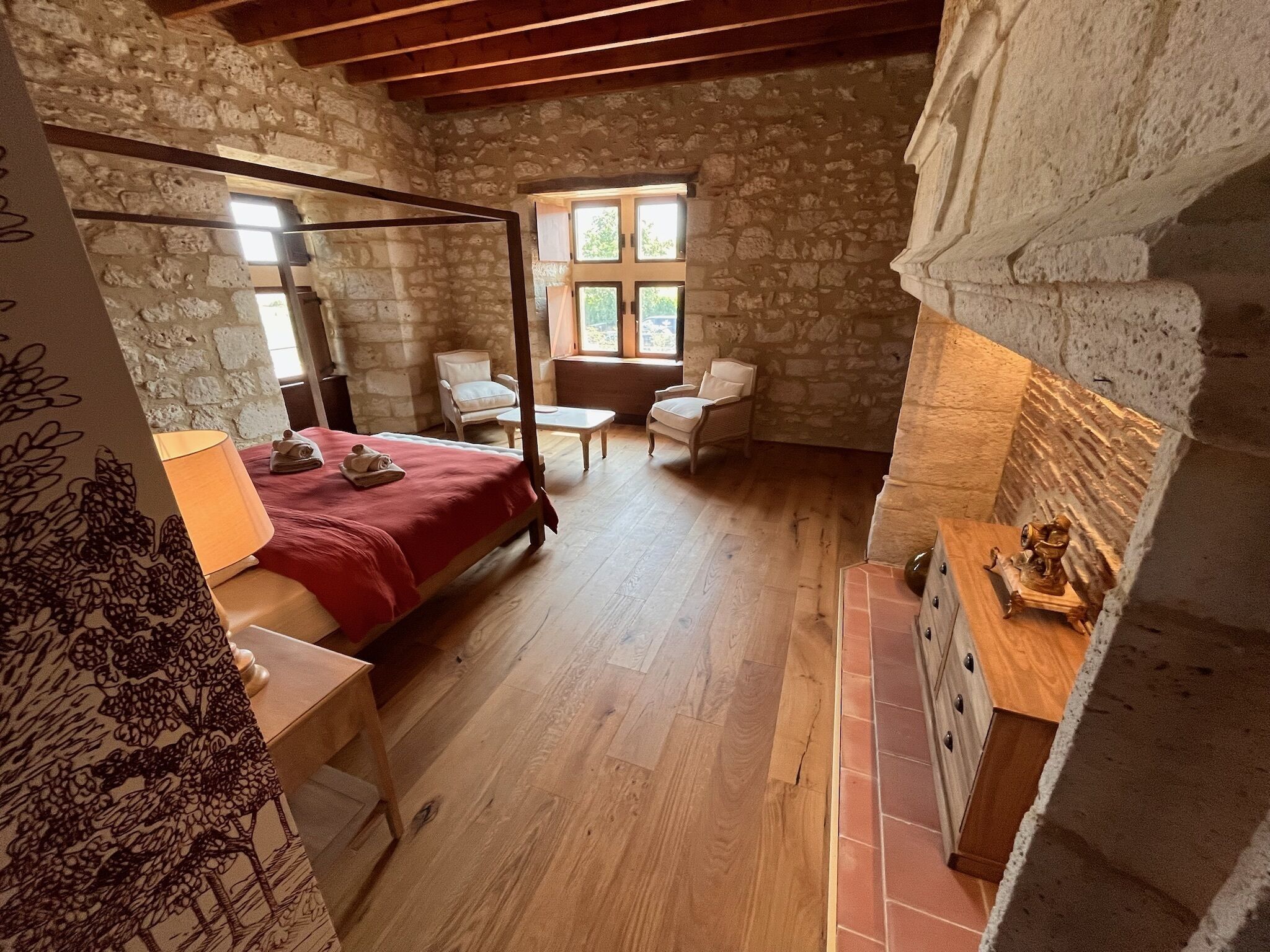 Un dormitorio con cama con dosel, suelo de madera, paredes de piedra y una ventana con vistas.