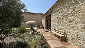 Un edificio de piedra con terraza de madera, asientos exteriores y una escalera que lleva a la entrada.