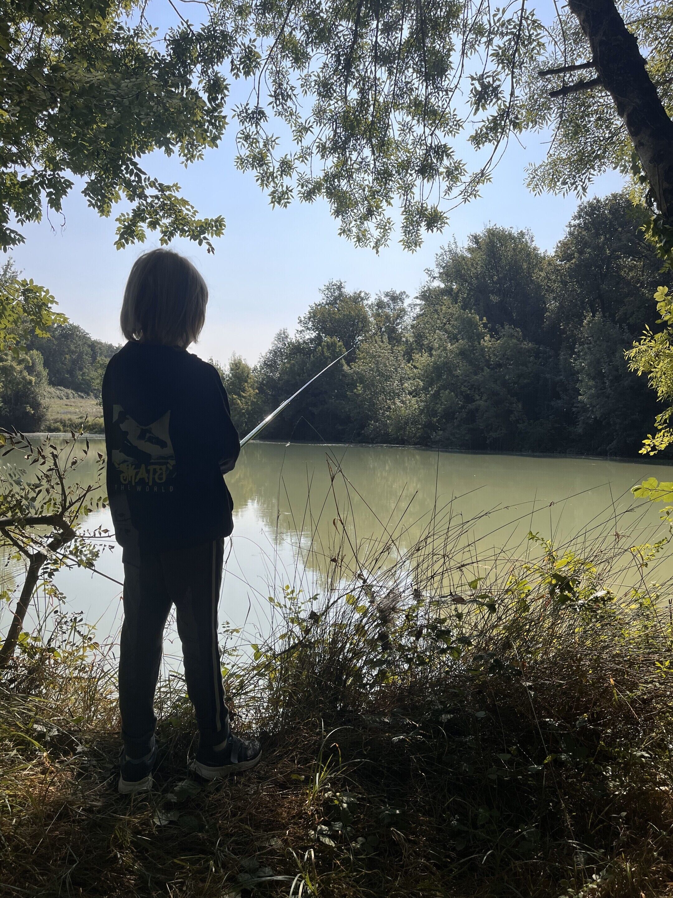 A person fishing by a calm lake surrounded by trees.