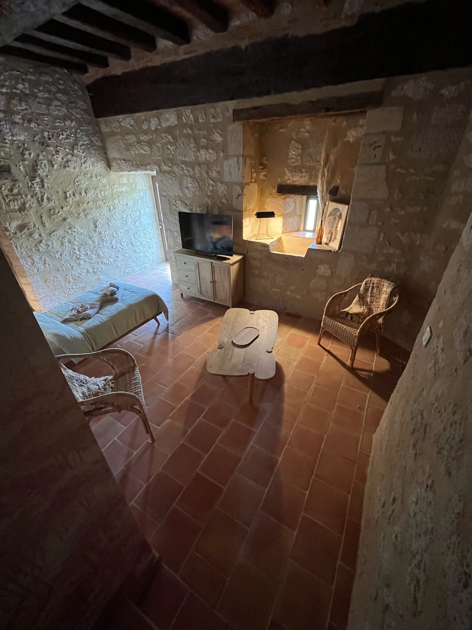 A rustic stone-walled room with a television, a small table, and two wicker chairs.