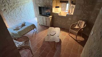 A rustic stone-walled room with a television, a small table, and two wicker chairs.
