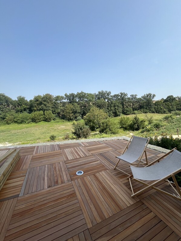 Una terraza de madera con dos sillones de descanso y un bajante.